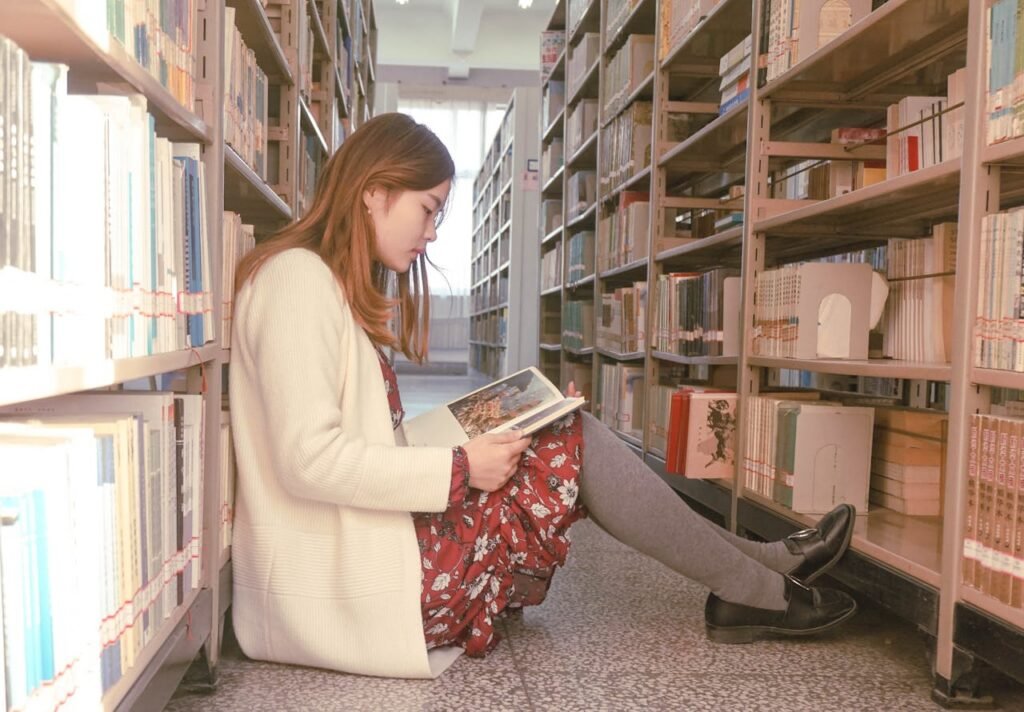 Chica sentada en el suelo en una biblioteca leyendo un libro