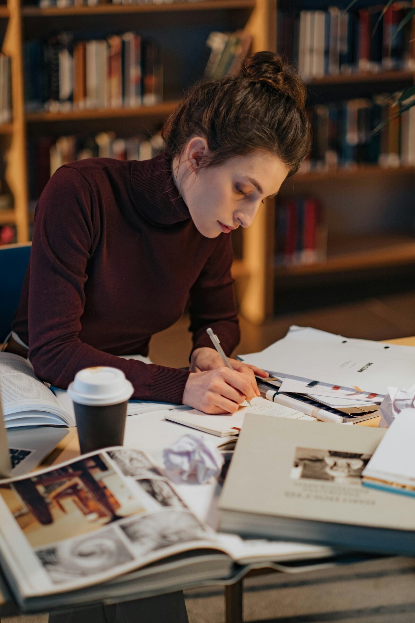 Una chica sentada en un escritorio con papeles, cuadernos y un café escribiendo